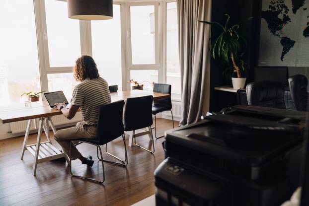Young man using laptop and earphones while sitting by table in office