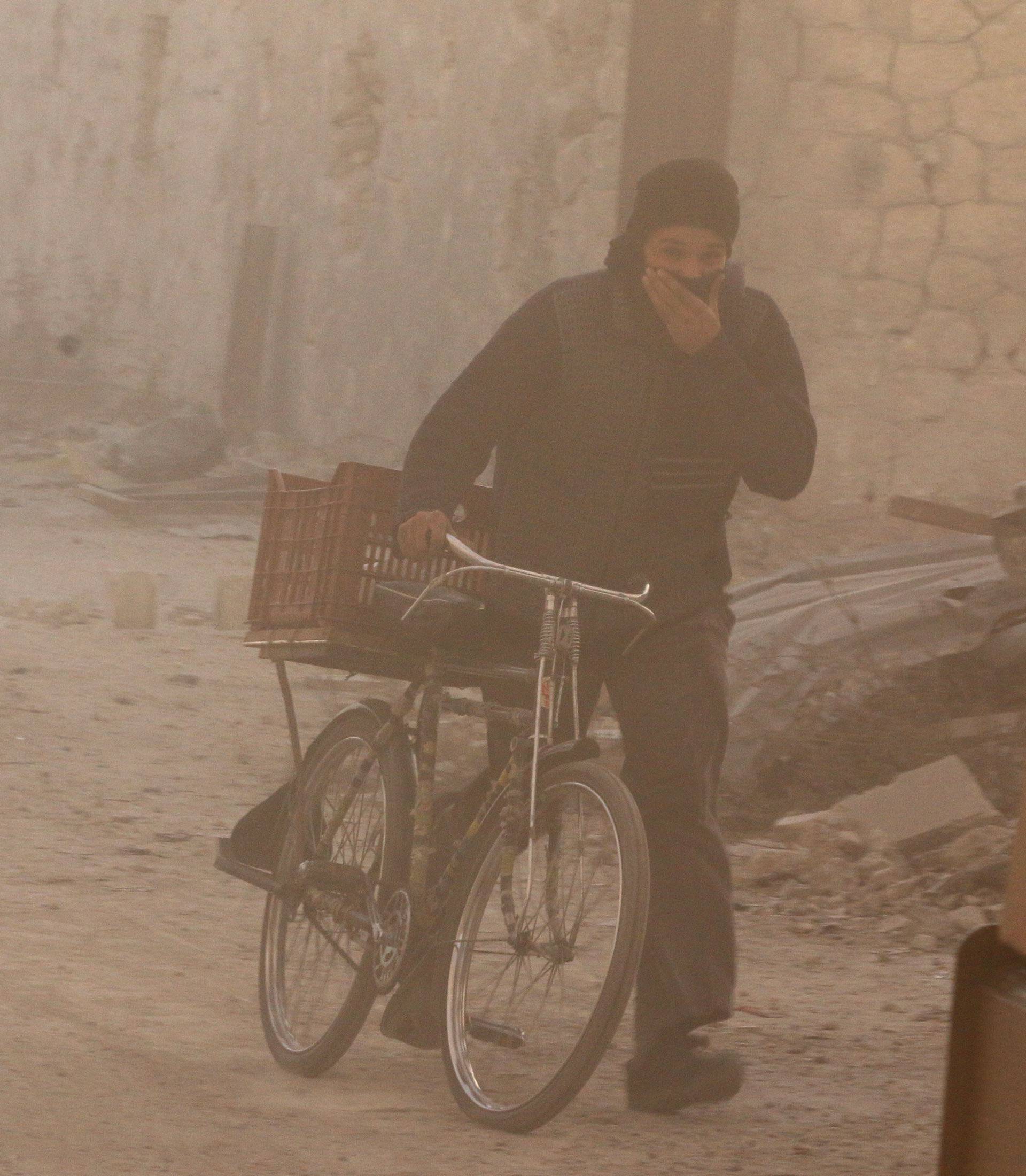 A man covers his face from dust as he walks with a bicycle after a strike on the rebel held besieged al-Shaar neighbourhood of Aleppo