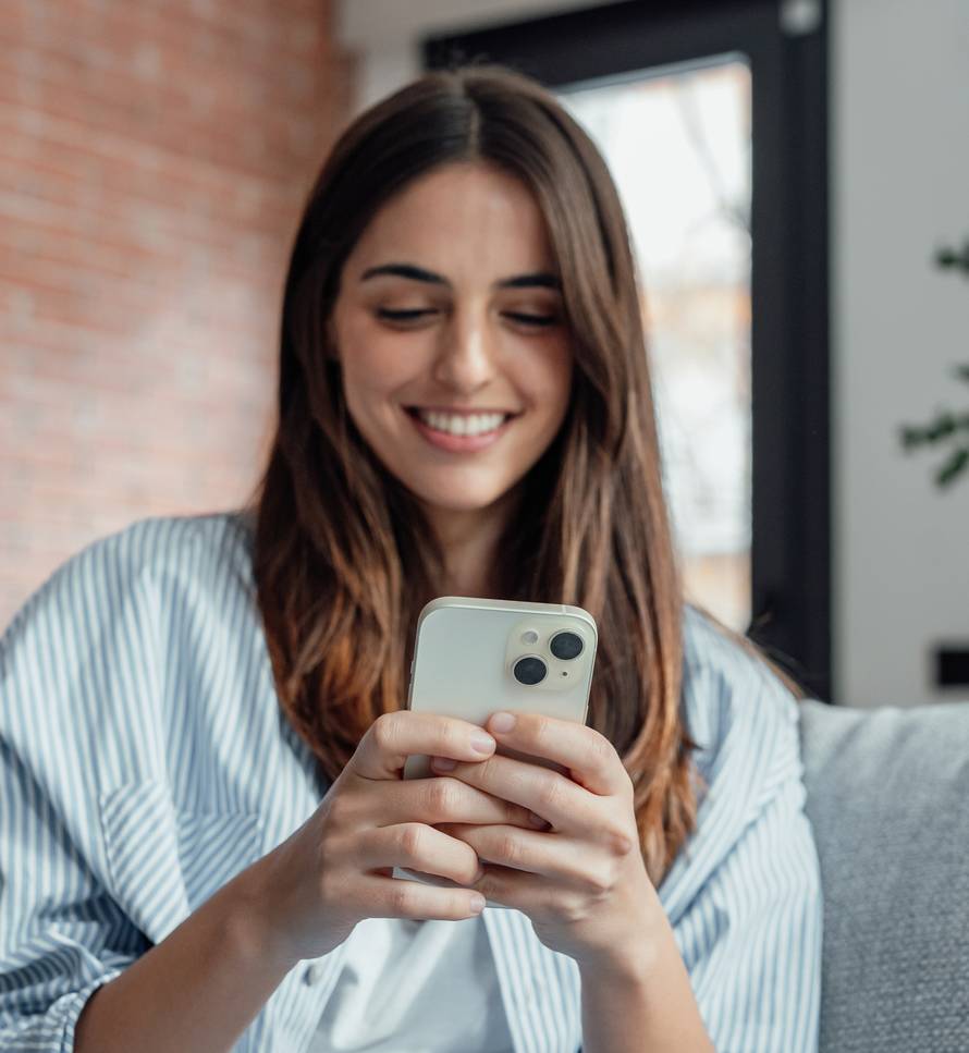 Smiling,Woman,Looking,At,Smartphone,Screen,,Sitting,On,Couch,,Enjoying