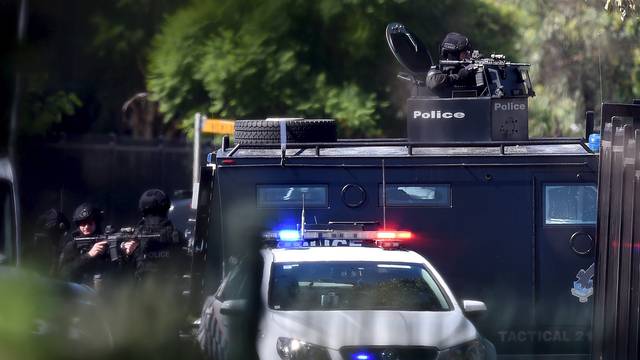 Heavily armed tactical police officers aim their weapons at the scene of a shooting in the western Sydney suburb of Ingleburn, Australia