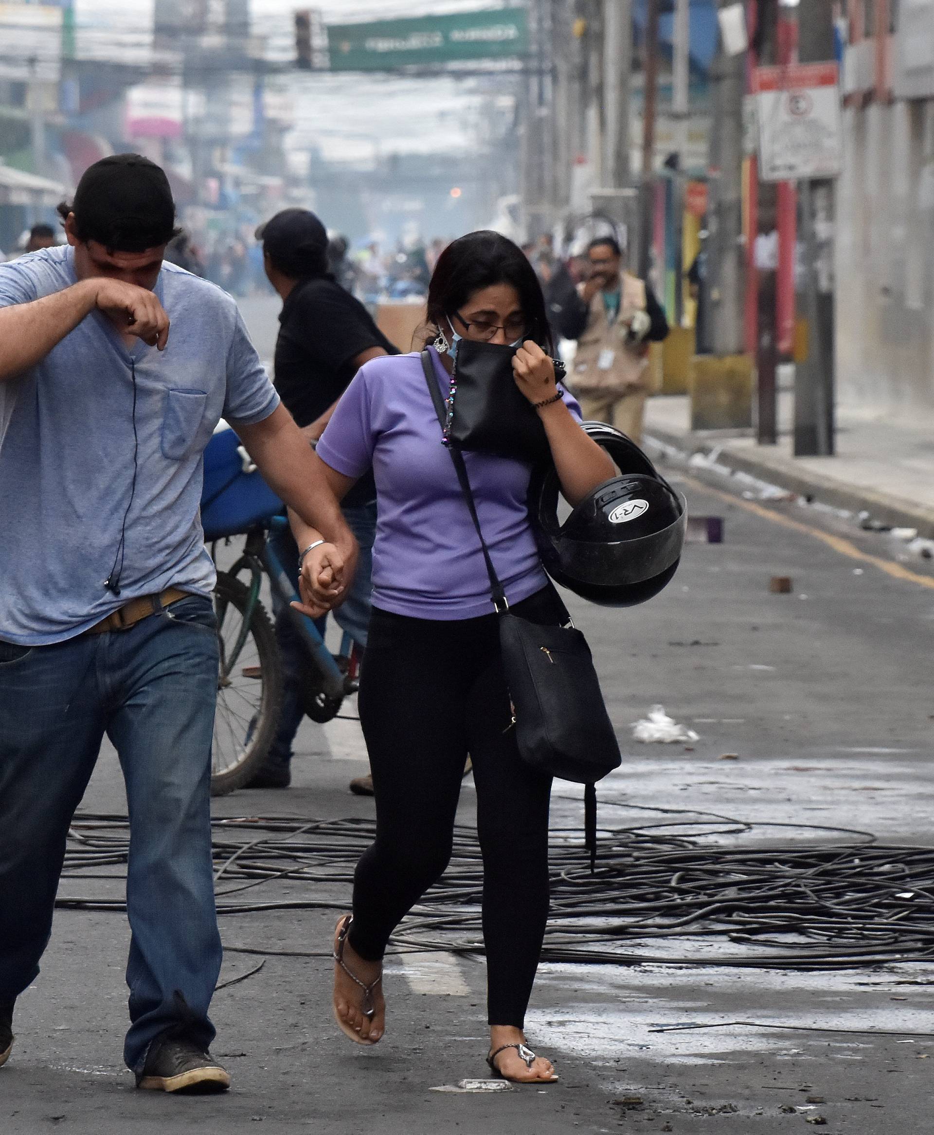 People overcome by tear gas walk away from clashes between supporters of Nasralla and police during a protest caused by the delayed vote count for the presidential election in San Pedro Sula