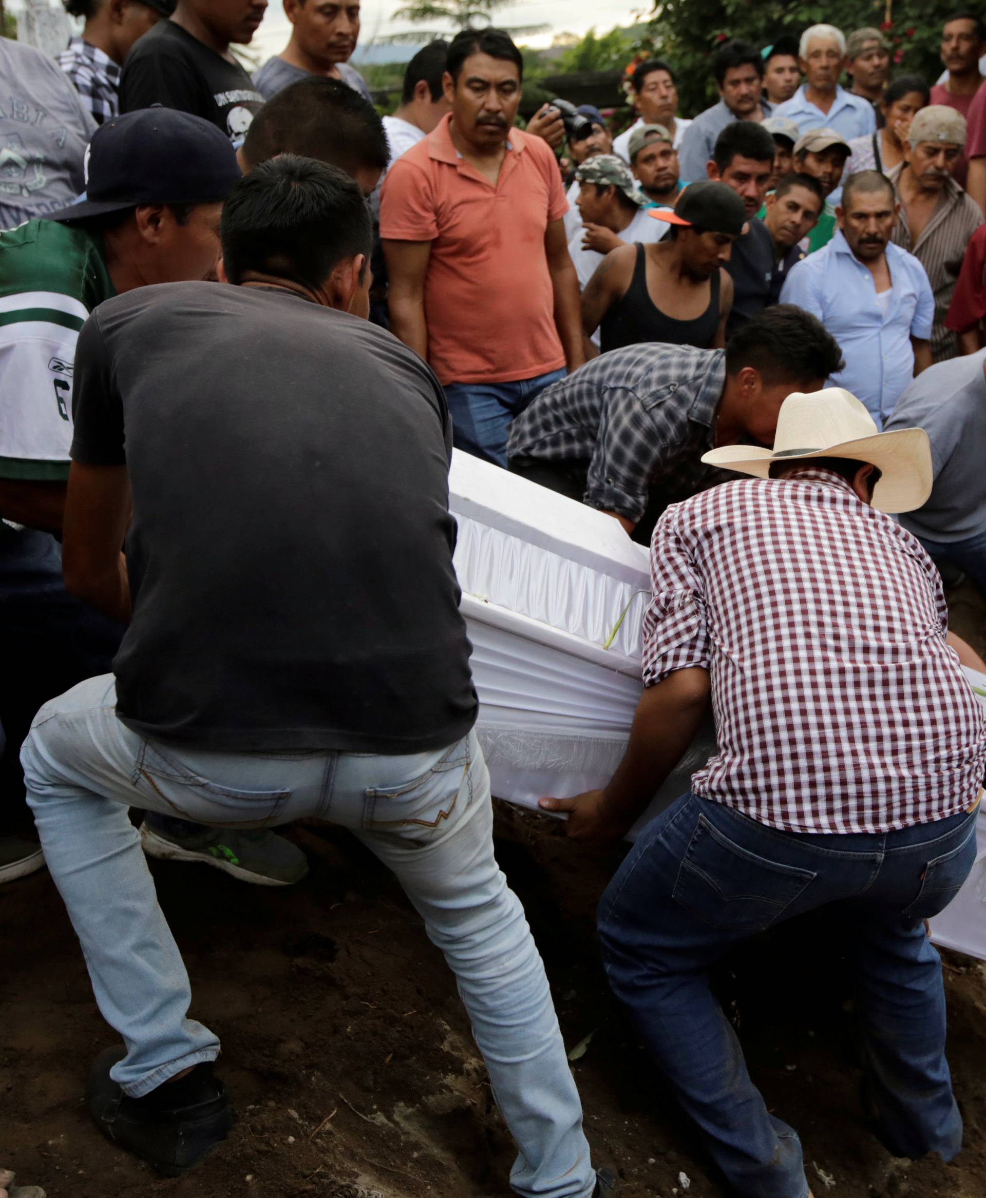 People lower casket of earthquake victim into grave, in Atzala