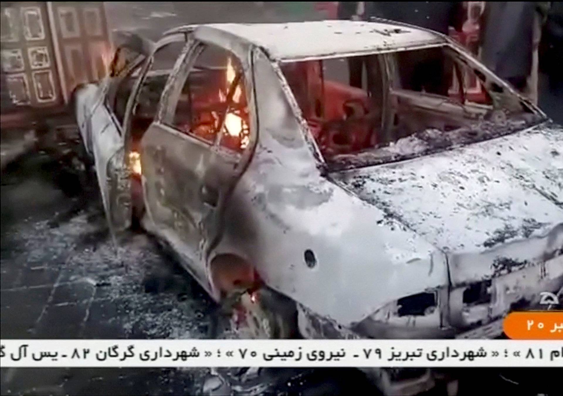 People stand near a burning car in Tuyserkan