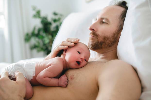 A father with a newborn baby in bed