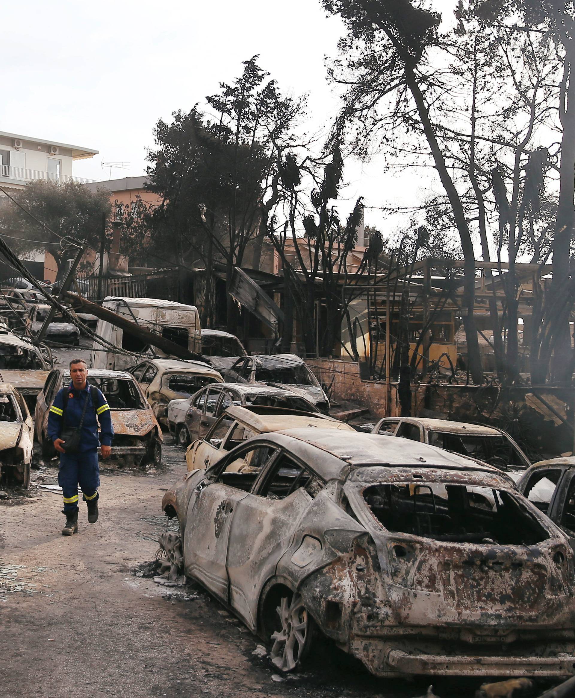 A firefighter walks among burned cars, following a wildfire at the village of Mati, near Athens