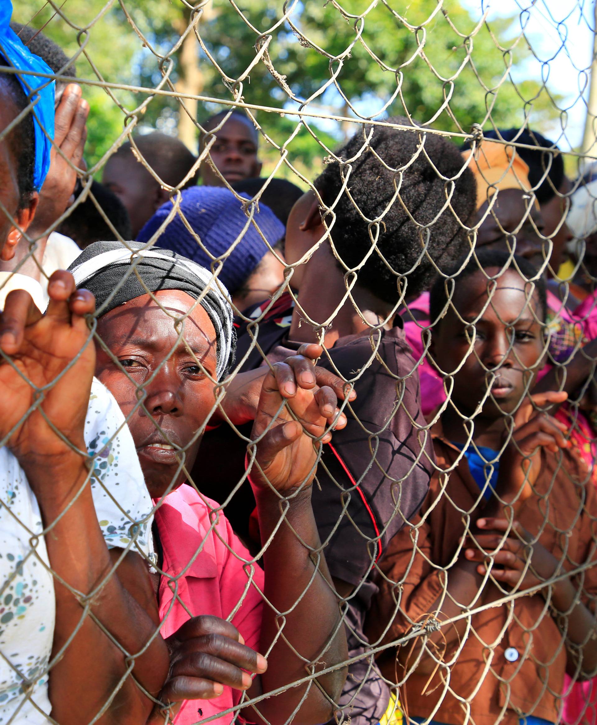 People gather at the perimeter fence to watch as rescue and recovery missions search for the bodies of dead passengers after a cruise boat capsized in Lake Victoria off Mukono district