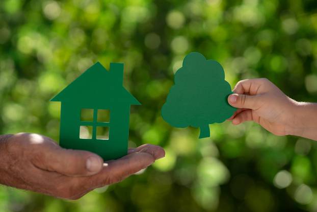 Family,Holding,Eco,House,In,Hands,Against,Spring,Green,Background.