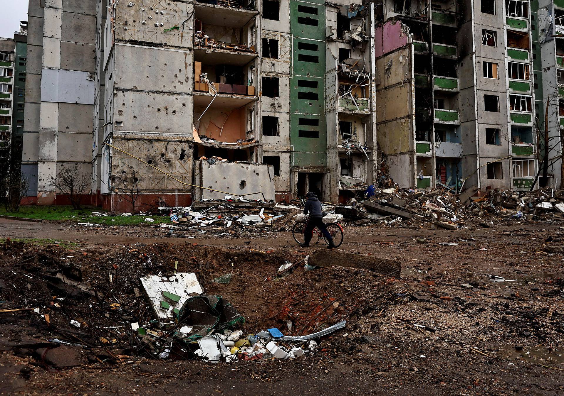 A man wheels his bicycle past a crater and a building destroyed by shelling, amid Russia's Invasion of Ukraine, in Chernihiv