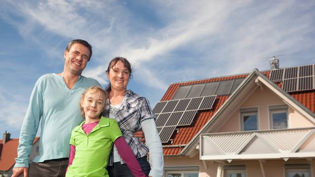 Happy,Family,Standing,In,Front,Of,House,With,Solar,Panels