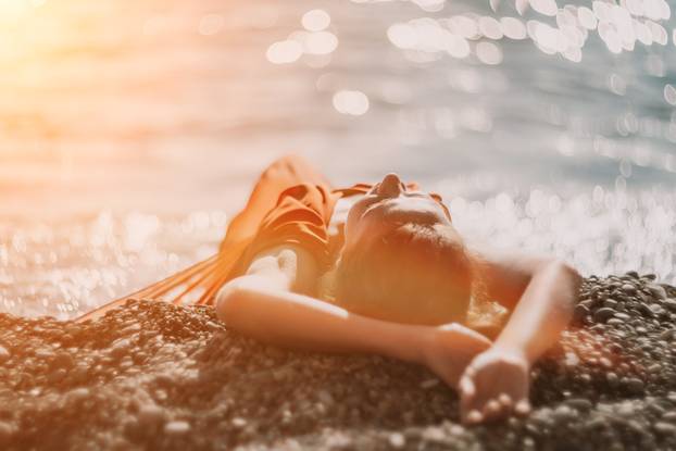 Woman in red dress on sea. Side view a Young beautiful sensual woman in a red long dress posing on the beach near sea on sunset. Girl on the nature on blue sky background. Fashion photo.