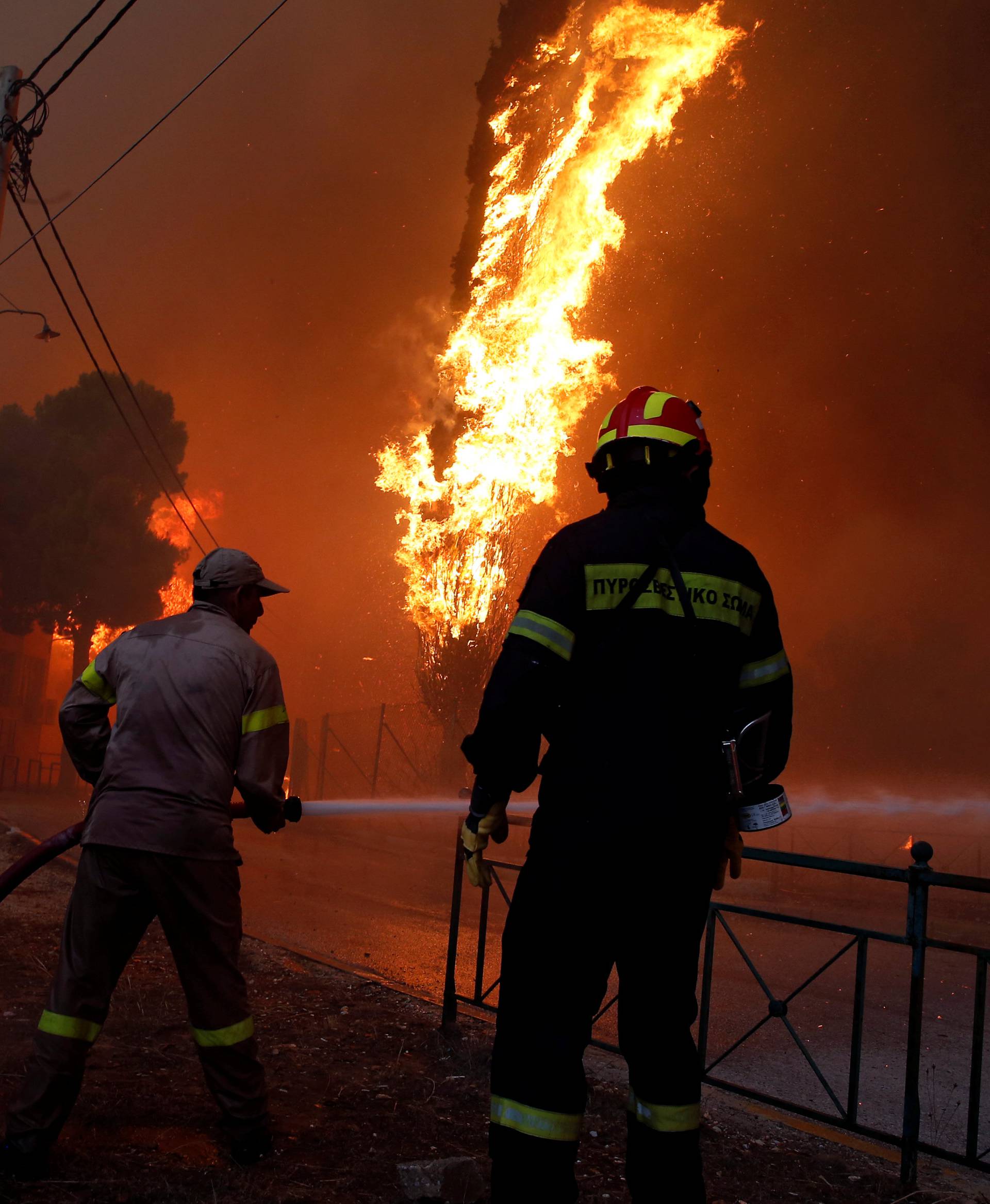 Firefighters and soldiers try to extinguish a wildfire burning in the town of Rafina, near Athens,