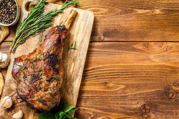 Roasted lamb, sheep leg on a cutting board with rosemary. wooden background. Top view. Copy space