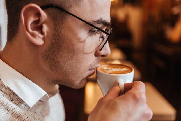 Young attractive man drinking coffee and looking aside.