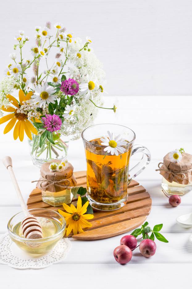Herbal tea with herbs and flowers in a glass tea pot with honey. Bouquet of flowers