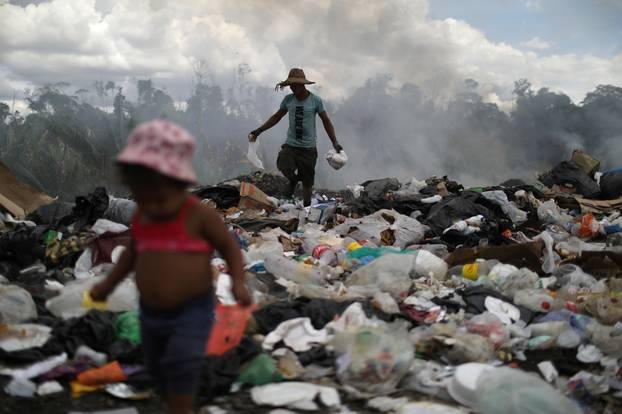 Venezuelan Antony Calzadilla is seen at a garbage dump as his child waits for him, in the border city of Pacaraima