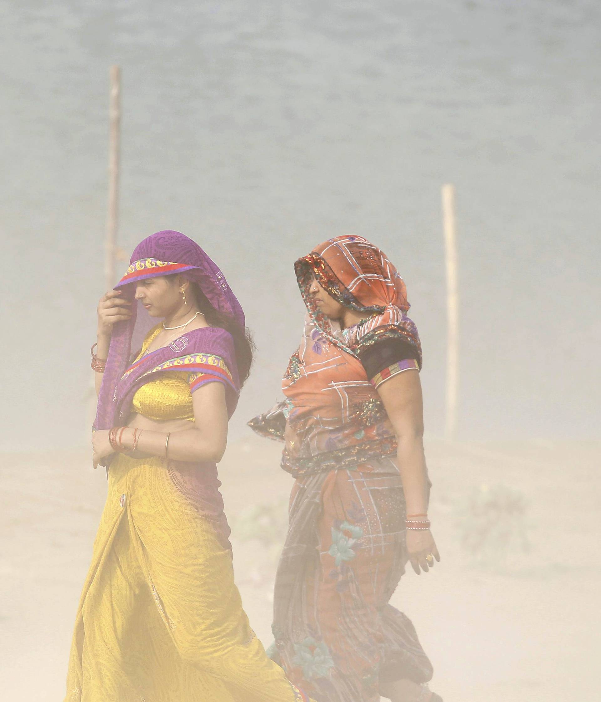Women cover themselves as they walk on the banks of the river Ganges during a dust storm in Allahabad