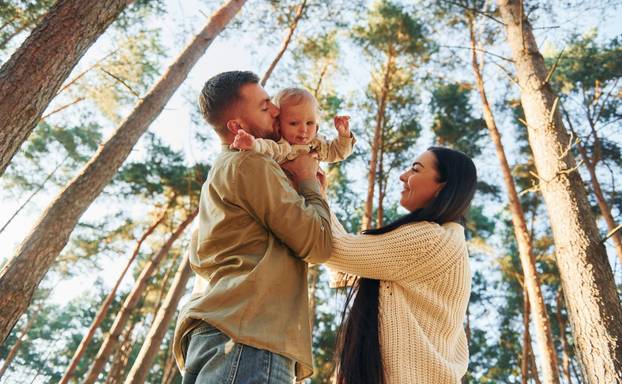 View from below. Happy family of father, mother and little daughter is in the forest