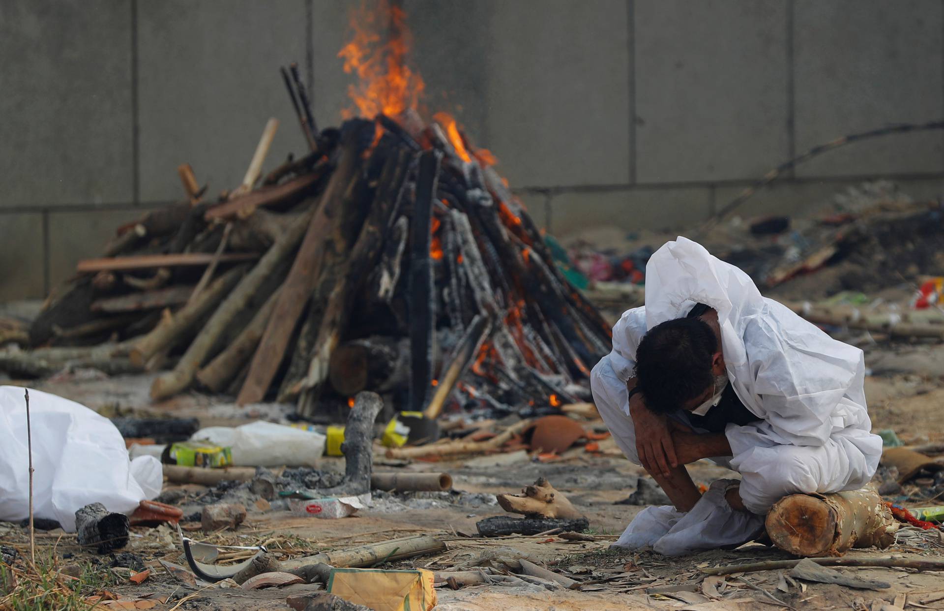 A man mourns as he sits next to the burning pyre of a relative, who died from the coronavirus disease (COVID-19), at a crematorium in New Delhi,