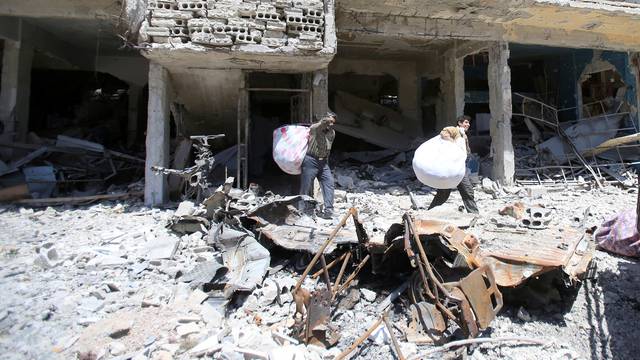 People hold belongings as they walk on the rubble of damaged buildings in the city of Douma, Damascus