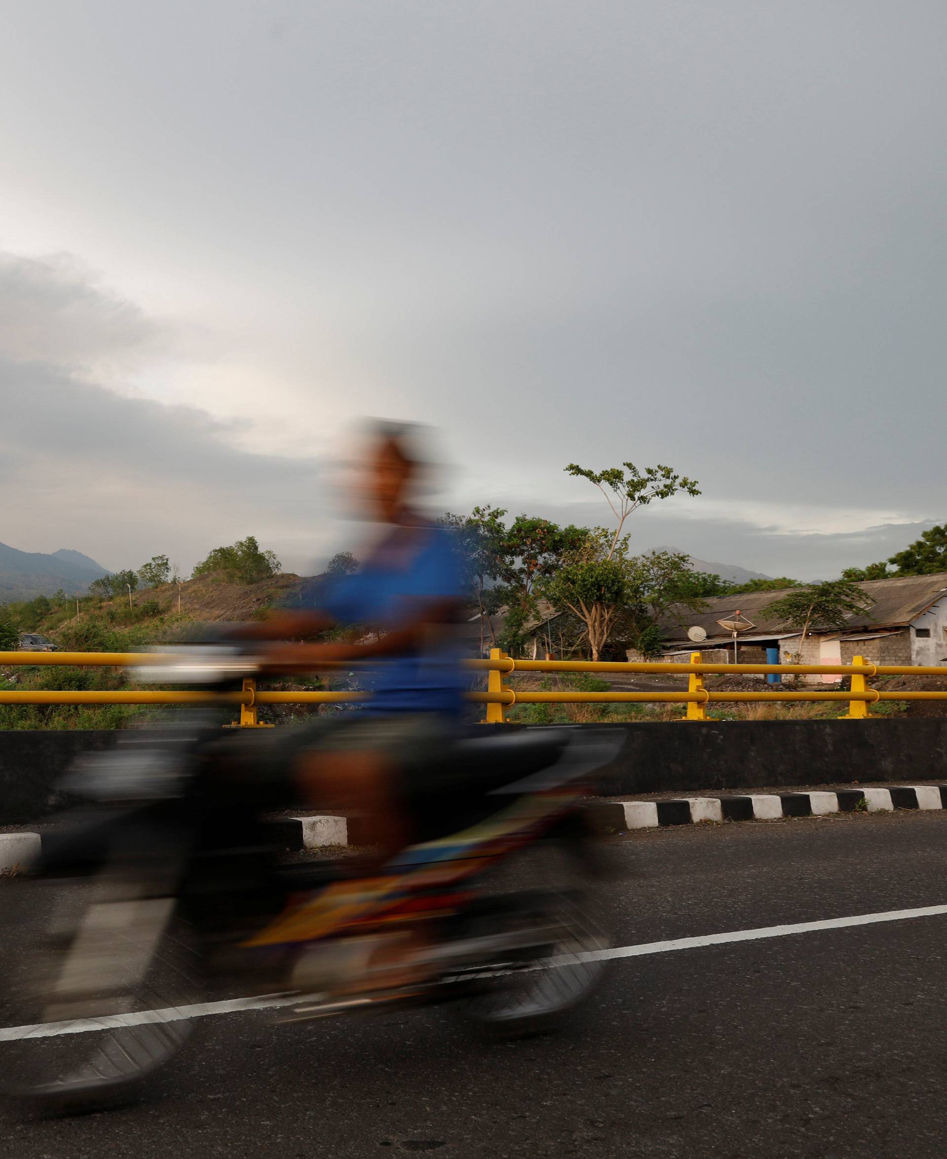 A motorist rides across a bridge as Mount Agung volcano erupts near Kubu in Bali