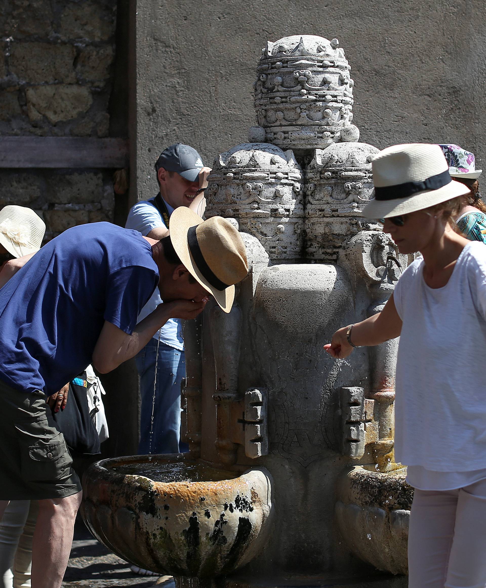 People cool themselves next to a fountain before Pope Francis leads his Sunday Angelus prayer in Saint Peter's square at the Vatican