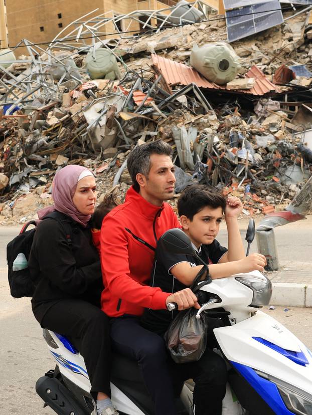A family rides past a damaged building as they return to their home, after a 10-day ceasefire between Lebanon and Israel went into effect, in the southern suburbs of Beirut