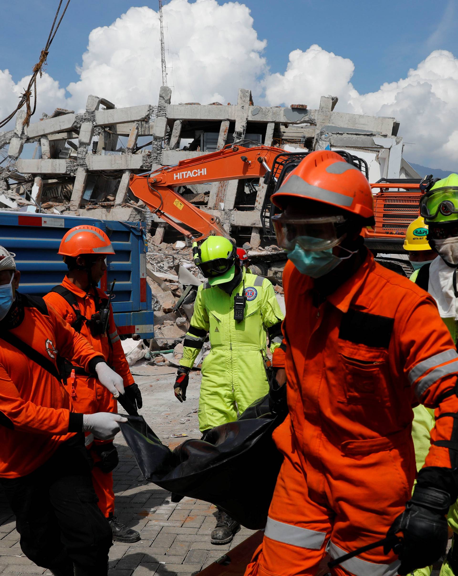 Rescue team members carry the dead body of a paraglider near the ruins of Roa-Roa hotel after the earthquake in Palu