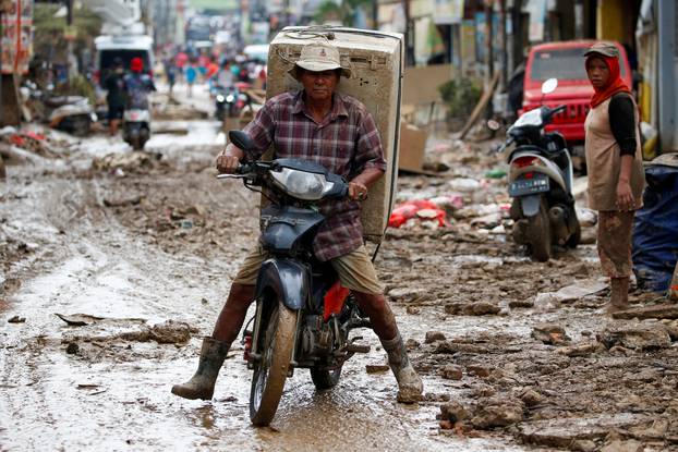 Man carrying a washing machine rides a motorbike as he collects items at a residential area affected by floods in Bekasi