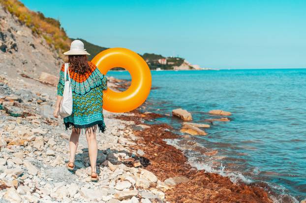A young woman is walking on a rocky wild beach with an inflatable circle in her hands. Concept of rest by the sea and travel. Close up