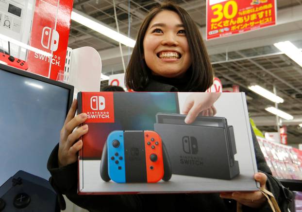 Nao Imoto smiles as she poses with her Nintendo Switch game console after buying it at an electronics store in Tokyo