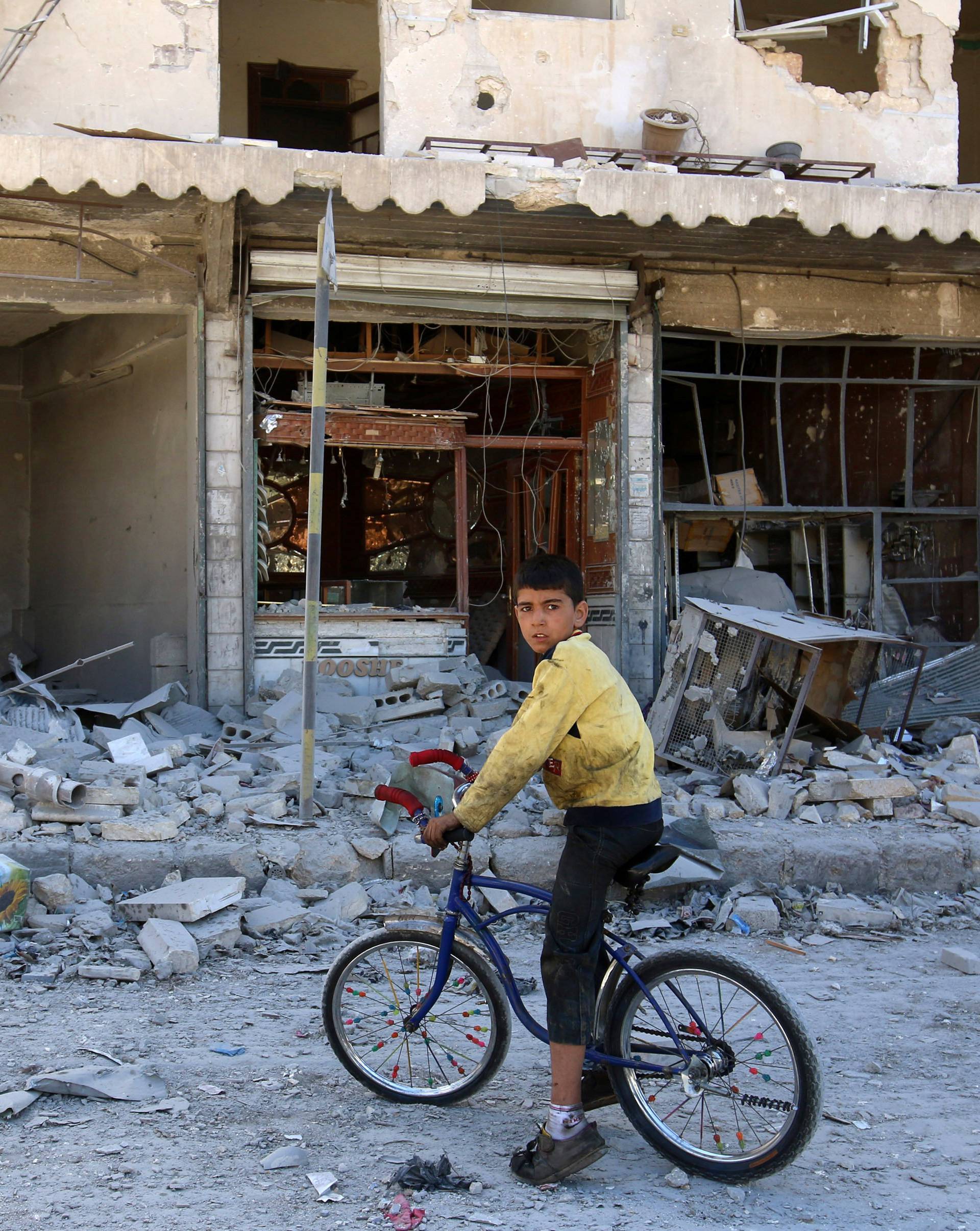 A boy sits on a bicycle in front of damaged shops after an airstrike on the rebel held al-Qaterji neighbourhood of Aleppo