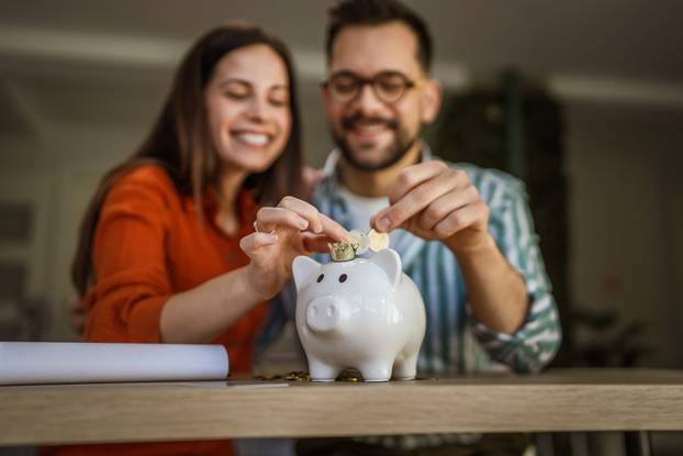 Cheerful,Young,Couple,Is,Smiling,While,Putting,Coins,Into,A