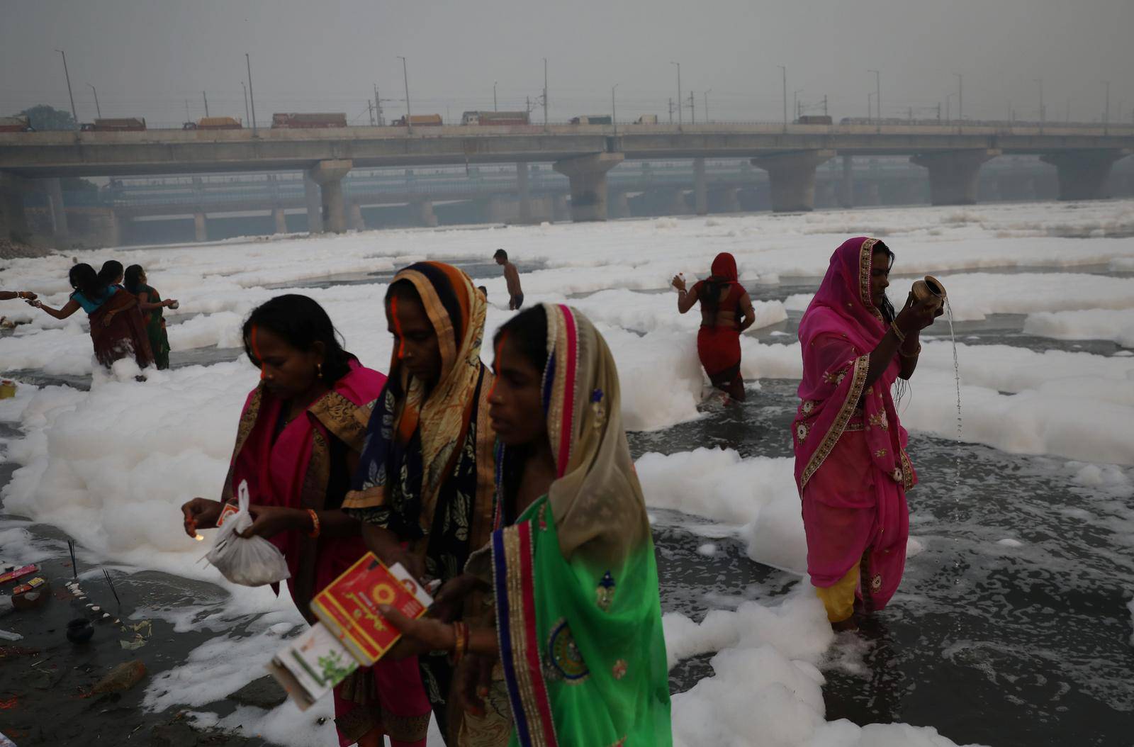 Women pray as they stand amidst the foam covering the polluted Yamuna river on a smoggy morning in New Delhi