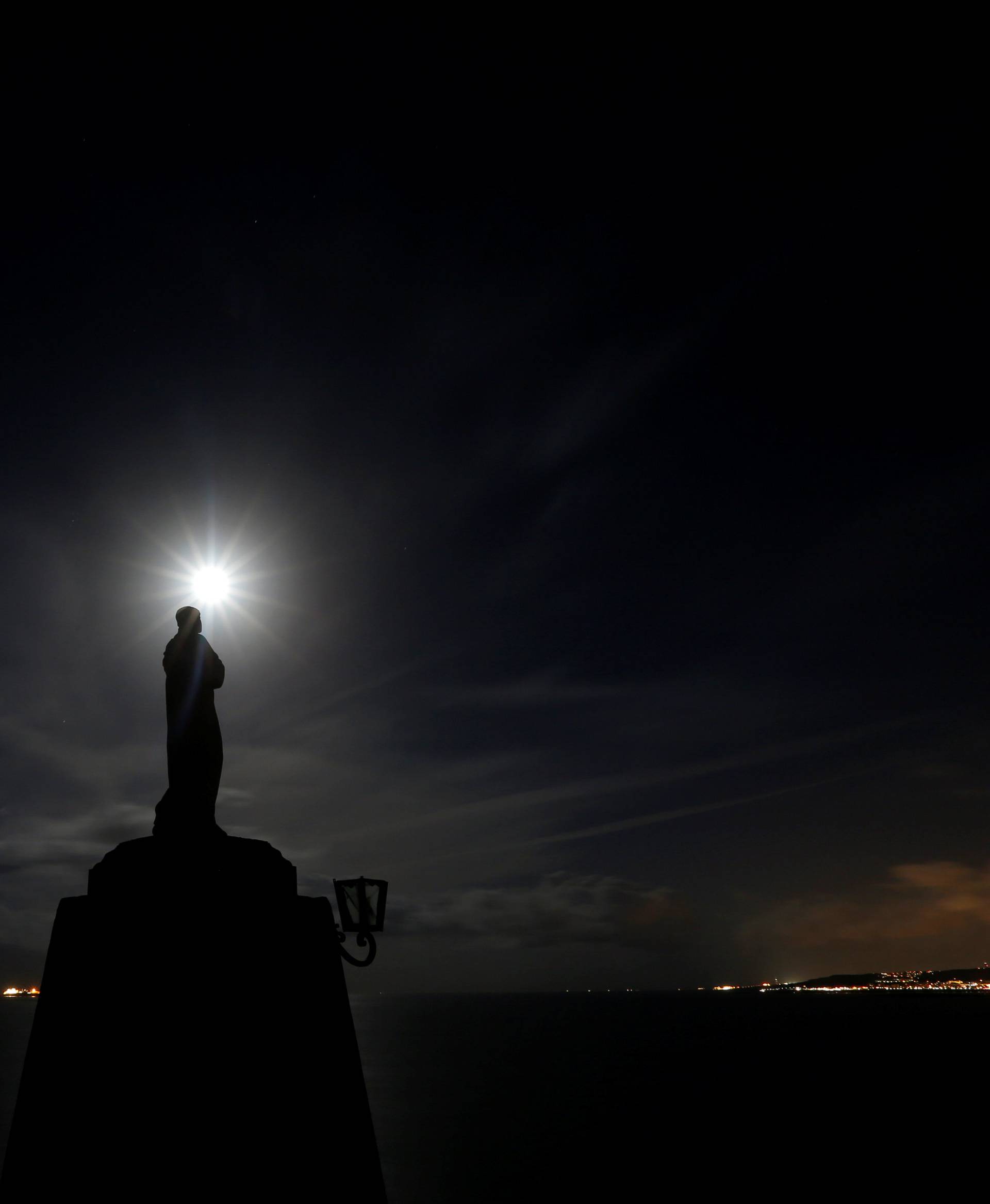 A statue of the Madonna overlooks the sea as the  supermoon rises and a lightning storm strikes off the coast at Marfa Ridge, in the north of Malta,