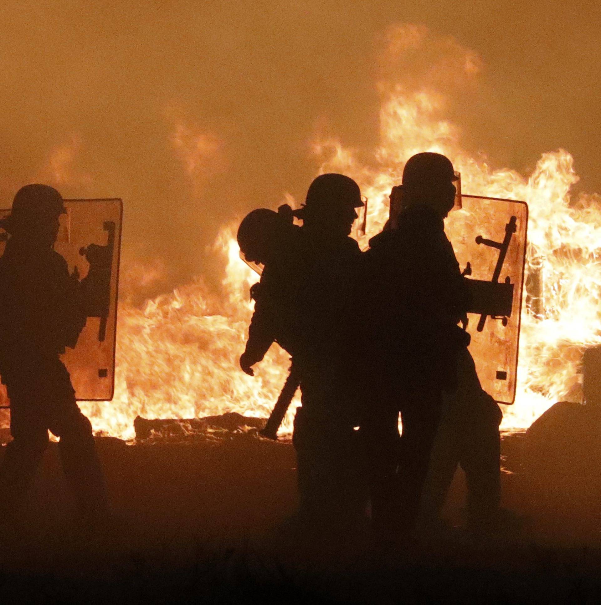 French CRS police are seen in silhouette with flames from burning debris on the eve of the evacuation and transfer of migrants to reception centers in France, and the dismantlement of the camp called the "Jungle" in Calais