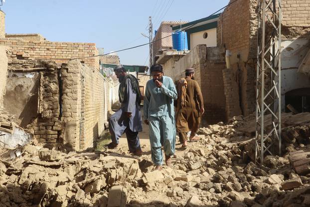 Residents walk amid the rubble of damaged houses along a street following an earthquake in Harnai