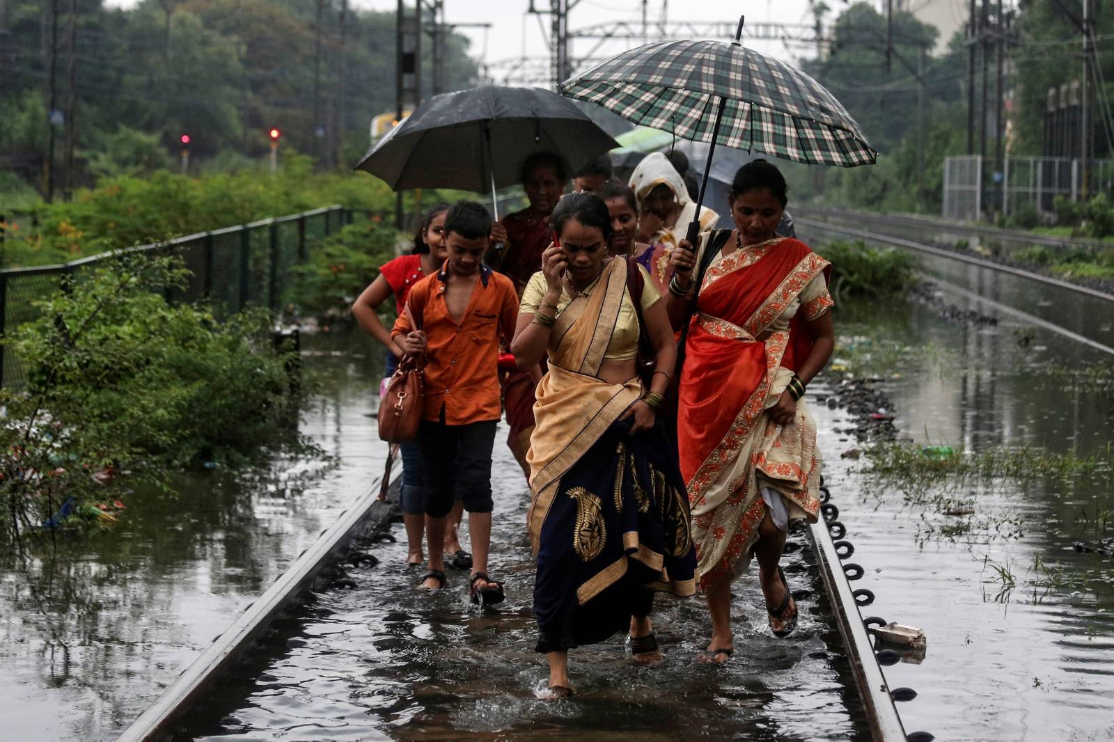 Commuters walk on waterlogged railway tracks after getting off a stalled train during heavy monsoon rains in Mumbai