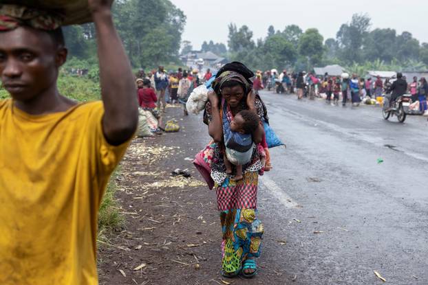 A woman carries her child and a bag of her harvested potatoes while returning from the field, in Kibati