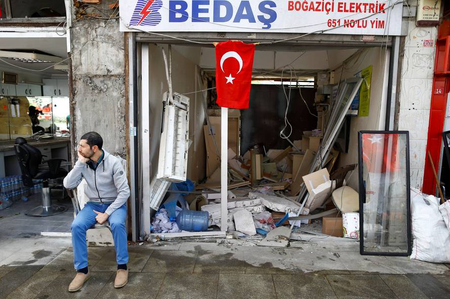 A man sits in front of a damaged shop near the scene of Tuesday's car bomb attack on a police bus, in Istanbul