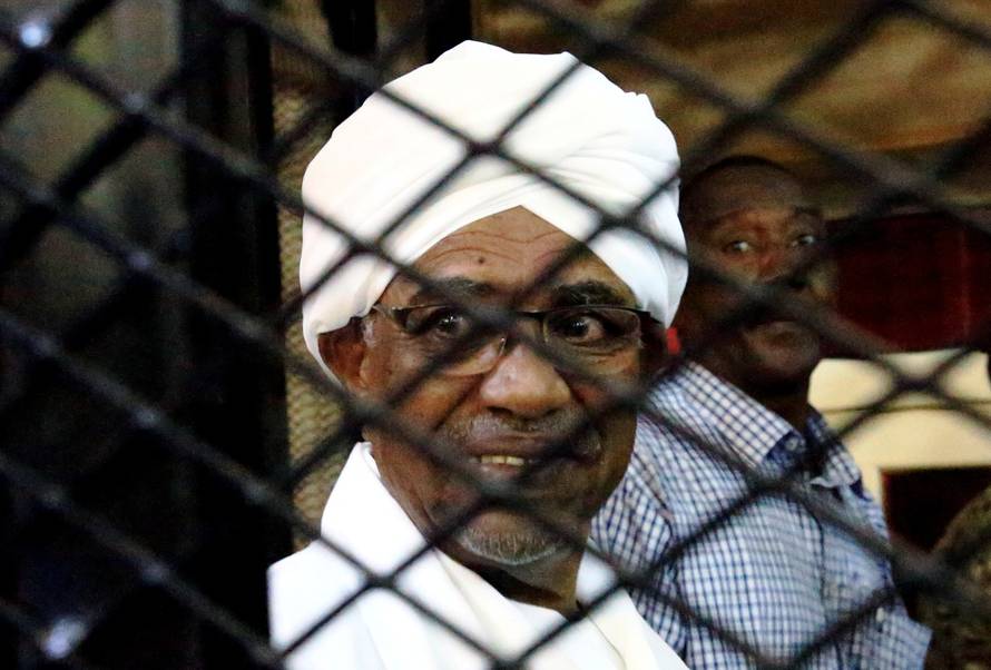 FILE PHOTO: Sudanese former president Omar Hassan al-Bashir smiles inside a cage as he faces corruption charges in a court in Khartoum