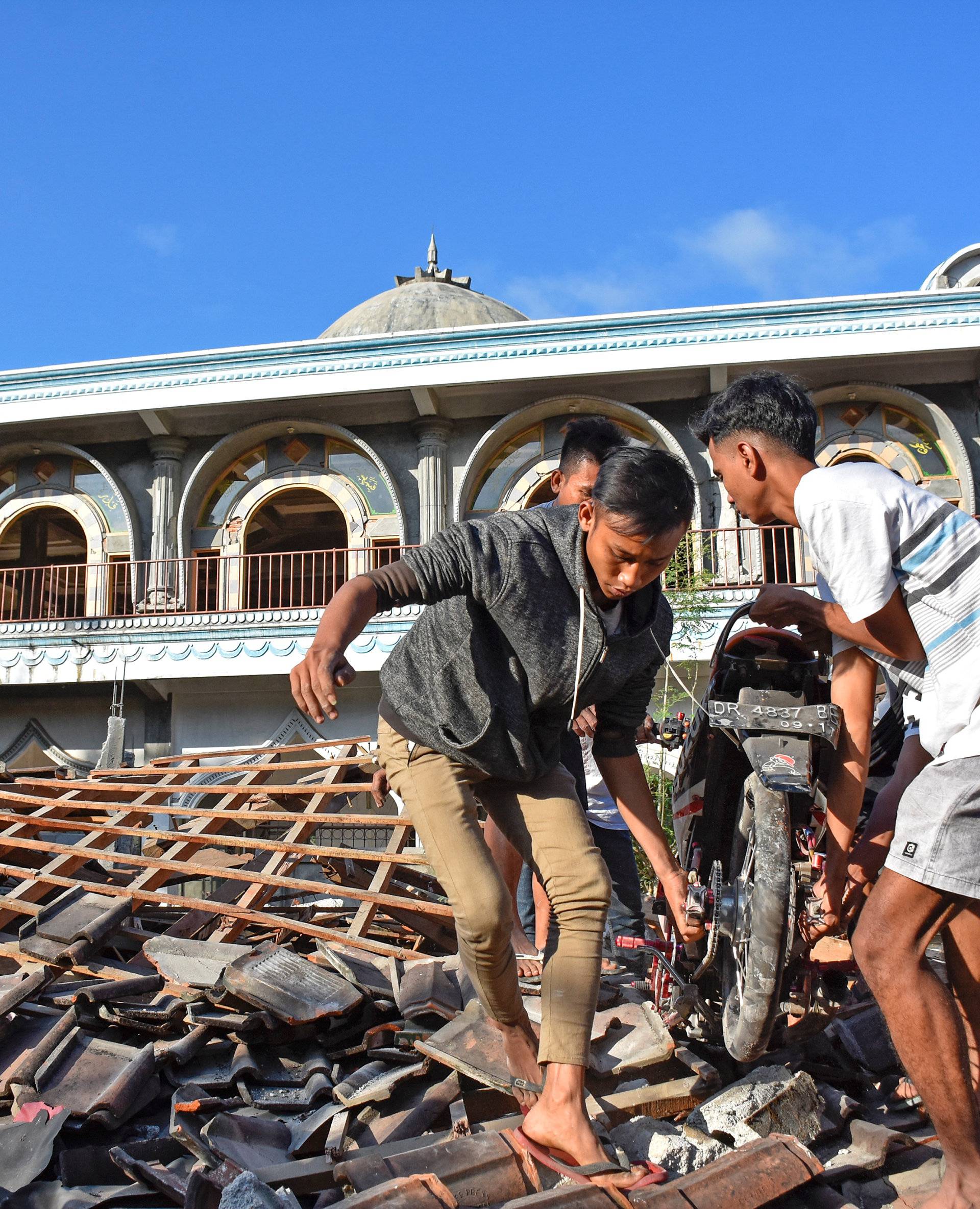 People recover a motorcycle from a damaged home near a mosque after a strong earthquake in  Gunungsari, West Lombok