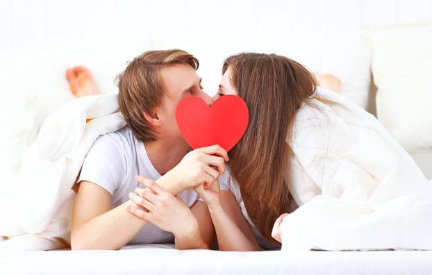 lover couple kissing with a red heart in bed