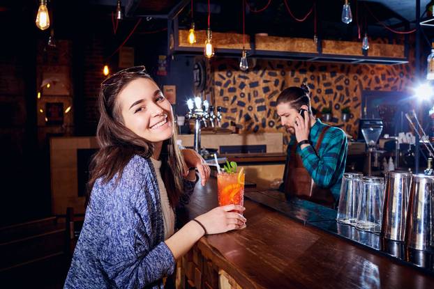 A girl with  cocktail smiles behind counter at the bar