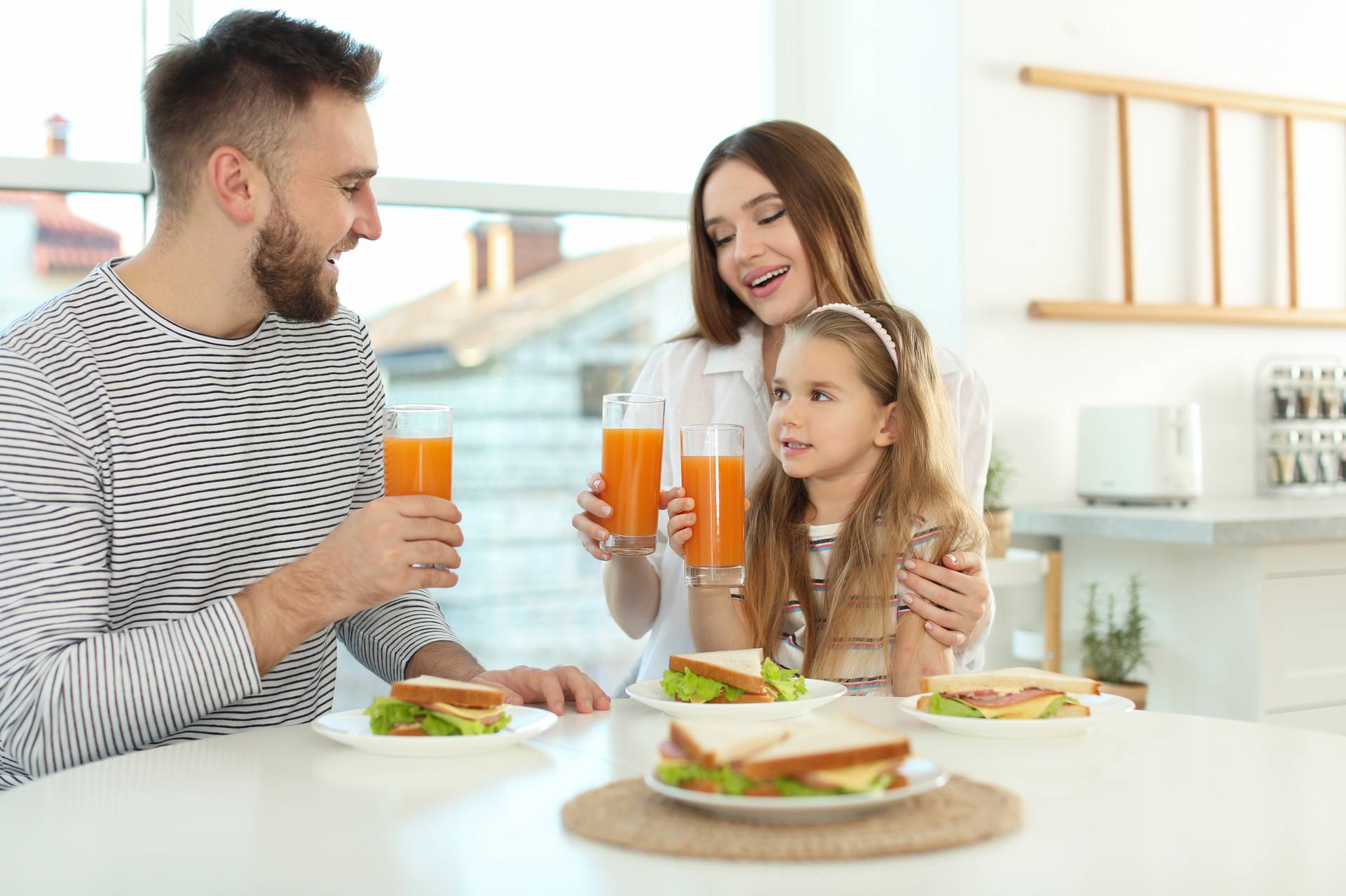 Happy family having breakfast with sandwiches at table in kitche
