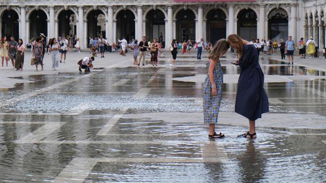 Tourists stand in flooded St. Mark's Square during high tide, in Venice