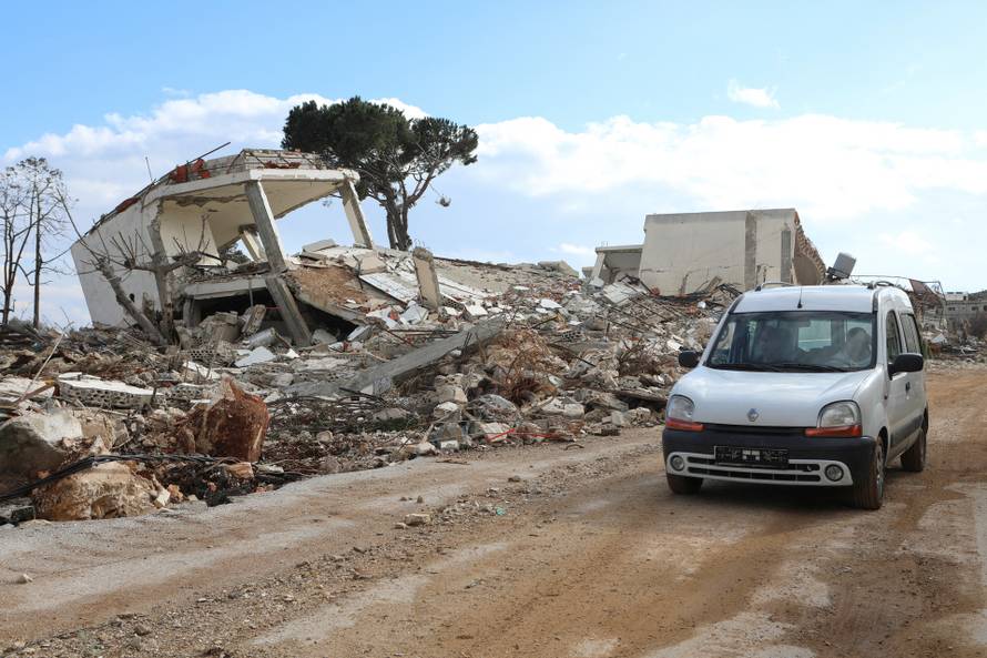People drive past a damaged site as residents return to the Lebanese village of Khiam