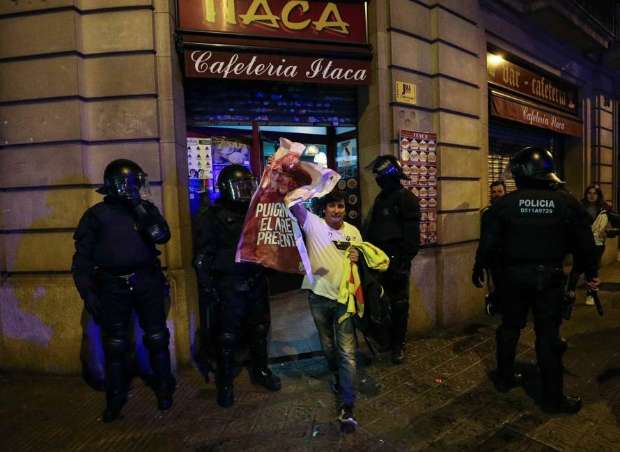 A protestor holds up a poster of former Catalan president Carles Puigdemont as he leaves a cafe during skirmishes with police after Puigdemont was detained in Germany,  in Barcelona