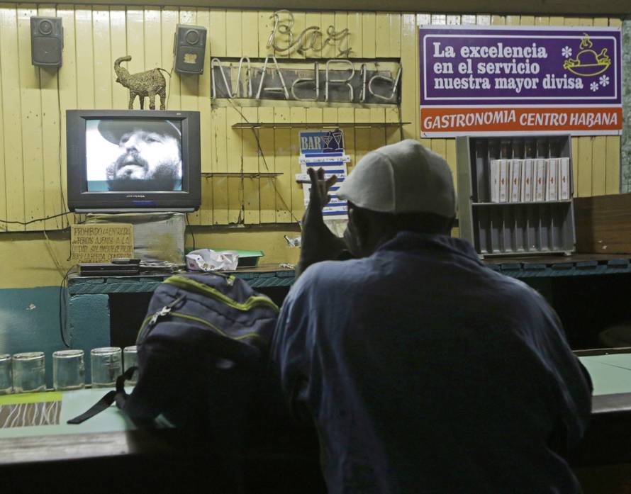 A man watches a television broadcast with the image of Cuba's former President Fidel Castro in Havana