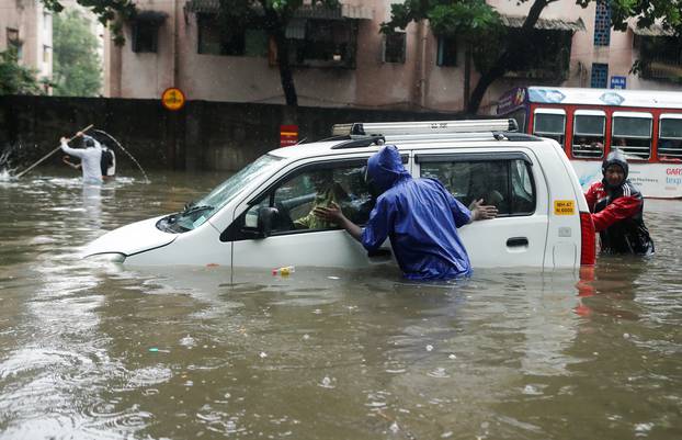 People push a car through a waterlogged street after it broke down during heavy rainfall in Mumbai