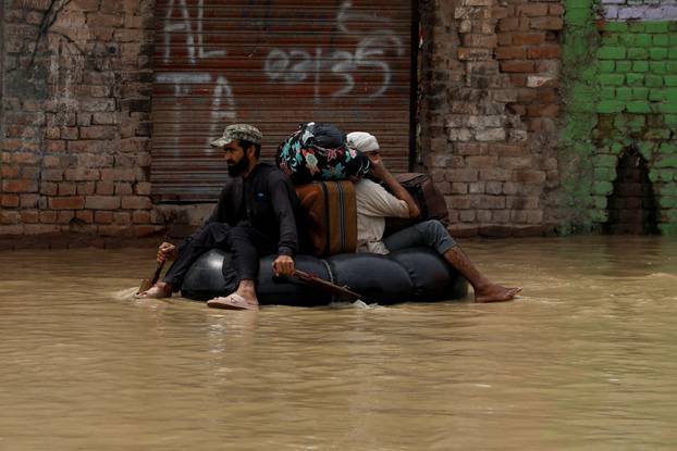 A volunteer paddles an inflatable tube as he evacuates a flood victim with his belongings, following rains and floods during the monsoon season in Charsadda